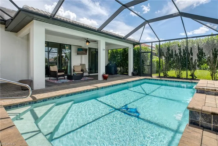Screened enclosure featuring a rectangular pool with integrated steps, surrounded by brick-patterned pavers and a tiled water line