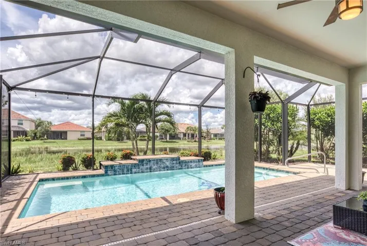 Screened lanai featuring a swimming pool, spa with a tile spillway, and paver decking