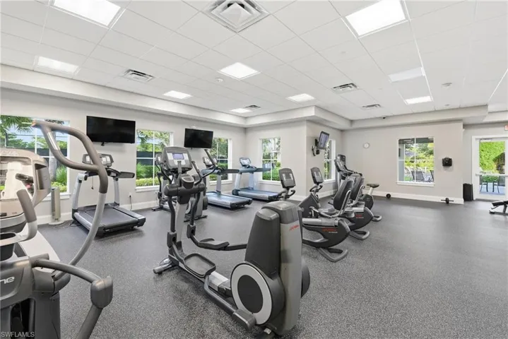 Fitness center featuring cardio equipment, multiple wall-mounted screens, recessed lighting, and large windows