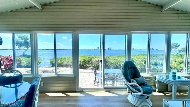 Sunroom with expansive water frontage, multiple sliding glass doors, horizontal paneling on walls, and wood-finish flooring