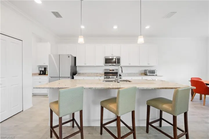 Kitchen with a kitchen island with sink, sink, white cabinets, pendant lighting, and appliances with stainless steel finishes