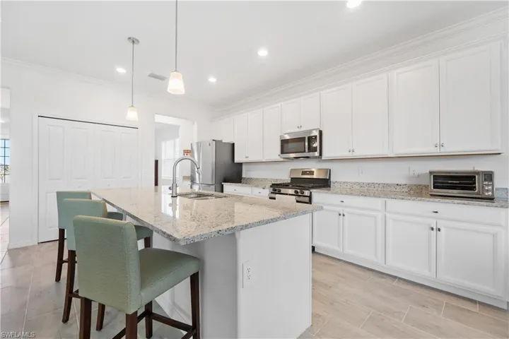Kitchen featuring appliances with stainless steel finishes, white cabinets, hanging light fixtures, and a center island with sink