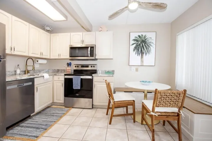 Kitchen featuring appliances with stainless steel finishes, light tile patterned flooring, light stone counters, and ceiling fan