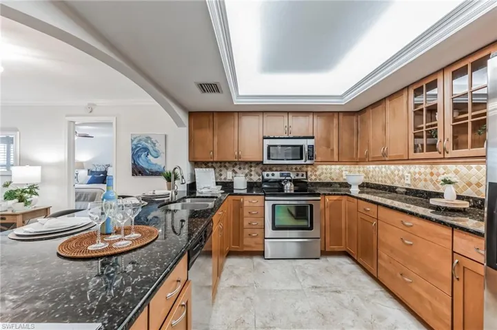 U-shaped kitchen featuring wood cabinetry, dark stone countertops, stainless steel appliances, and a tiled backsplash