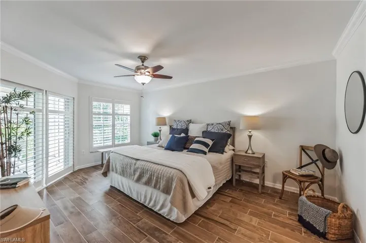 Bright bedroom featuring wood-finish flooring, white plantation shutters, a ceiling fan with integrated lighting, and crown molding