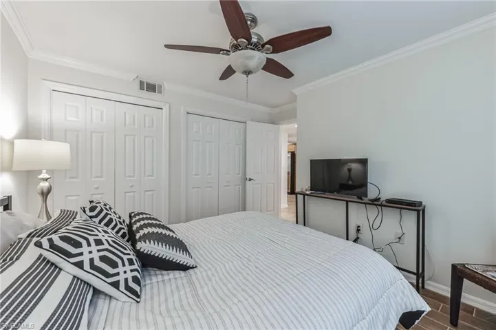 Bedroom featuring a ceiling fan with wood-finish blades, crown molding, white bi-fold closet doors, and wood-look flooring