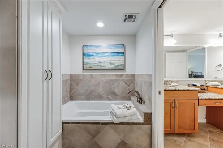 Built-in soaking tub with a tiled surround, recessed lighting, and integrated storage cabinetry