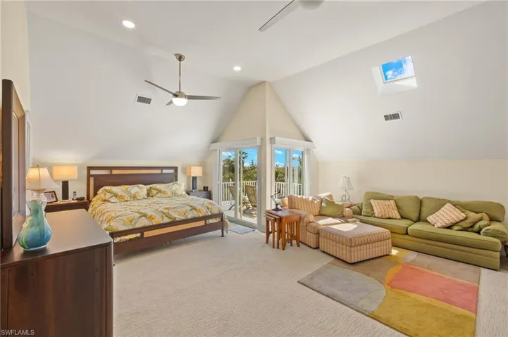 Carpeted bedroom featuring vaulted ceiling with skylight, access to exterior, and ceiling fan
