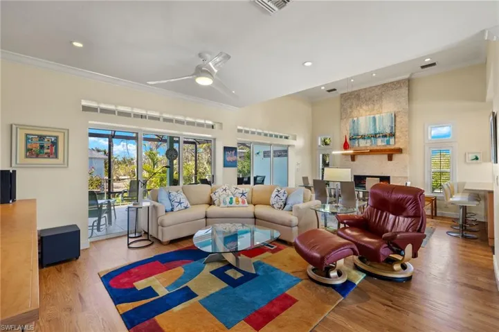 Living room with a large fireplace, ornamental molding, ceiling fan, hardwood / wood-style floors, and a high ceiling