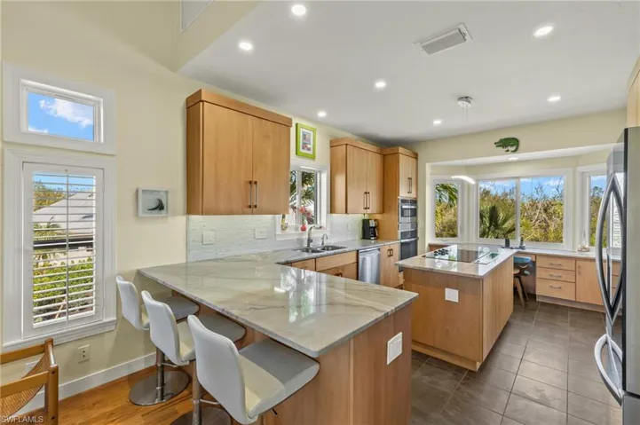 Kitchen with backsplash, stainless steel appliances, light stone countertops, a kitchen island, and kitchen peninsula