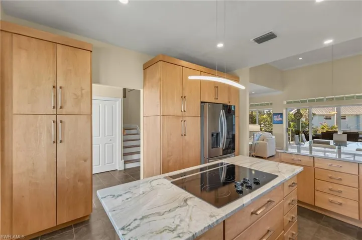 Kitchen with light stone countertops, black electric stovetop, light brown cabinets, and stainless steel fridge with ice dispenser