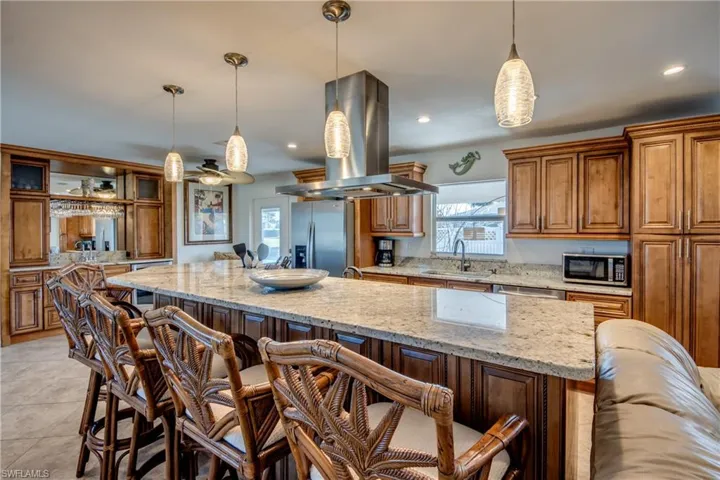 Kitchen featuring brown cabinetry, light stone counters, island range hood, a breakfast bar area, and healthy amount of natural light