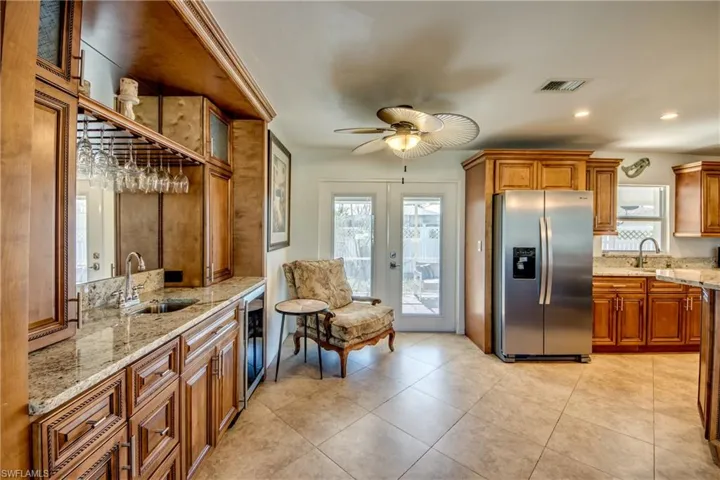 Kitchen featuring brown cabinetry, light stone counters, stainless steel refrigerator with ice dispenser, plenty of natural light, and recessed lighting