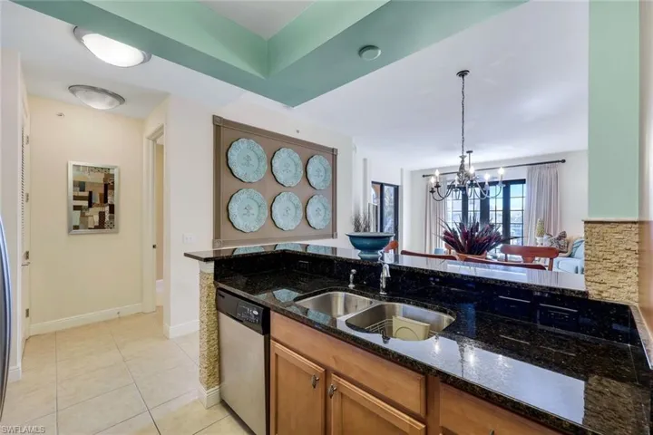 Kitchen with stainless steel dishwasher, dark stone counters, sink, a notable chandelier, and hanging light fixtures