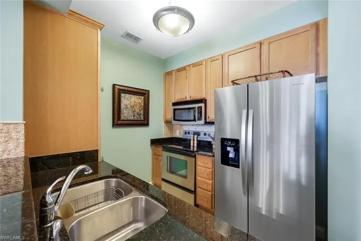 Kitchen featuring backsplash, sink, dark stone countertops, light brown cabinetry, and stainless steel appliances