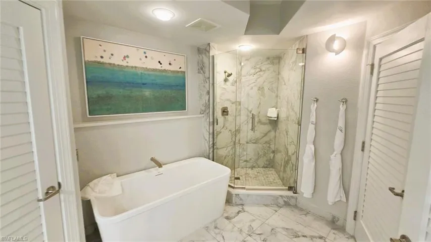 Full bath with marble look tile flooring, a marble finish shower, a freestanding tub, and a closet