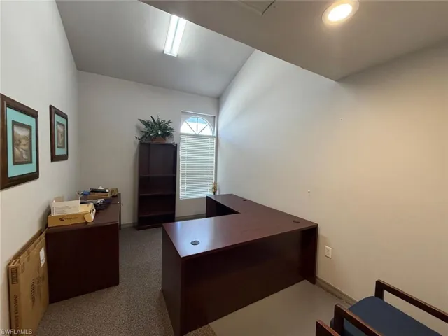 Office space with lofted ceiling and dark colored carpet