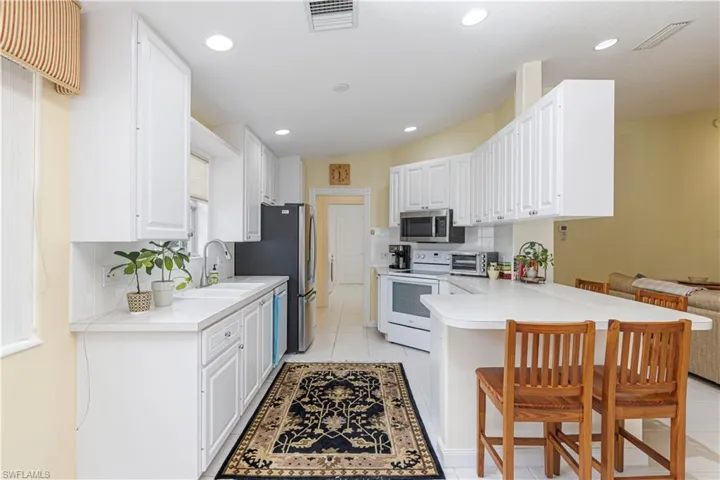 Kitchen featuring kitchen peninsula, a kitchen bar, stainless steel appliances, and white cabinetry