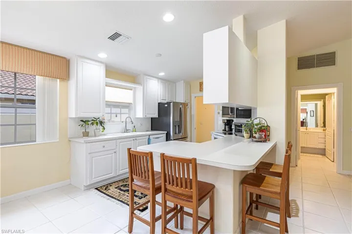 Kitchen featuring kitchen peninsula, sink, stainless steel fridge with ice dispenser, white cabinetry, and a breakfast bar area