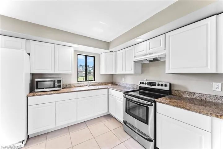 Kitchen featuring white cabinets, light tile patterned floors, appliances with stainless steel finishes, dark stone counters, and sink
