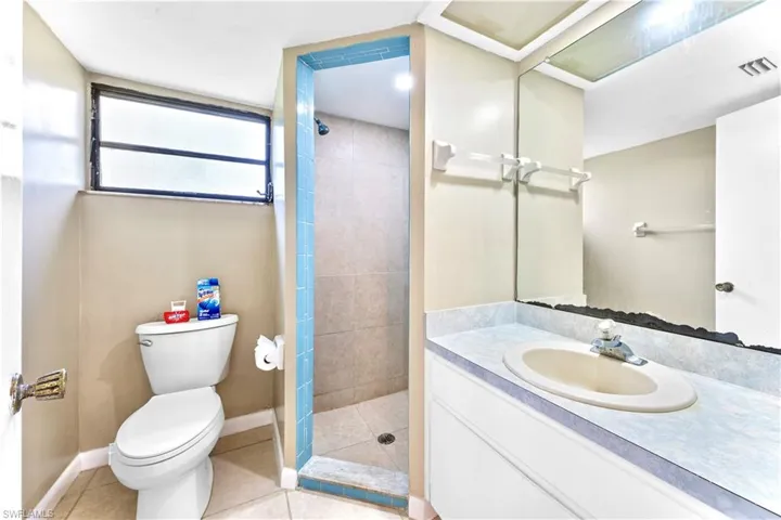 Bathroom with toilet, vanity, tile patterned floors, and tiled shower