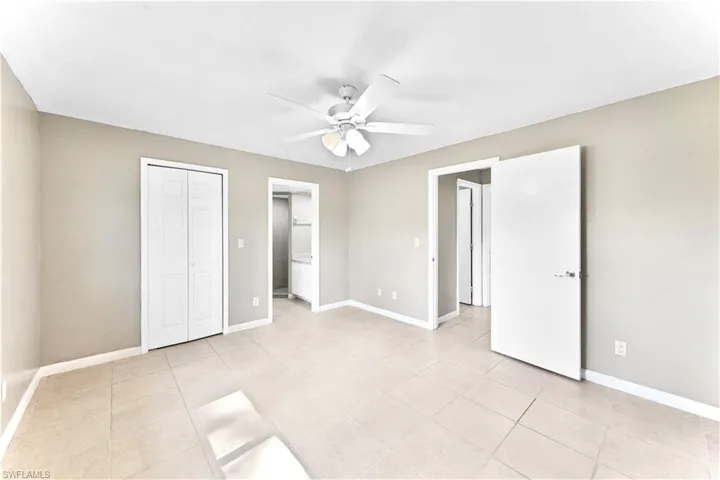 Unfurnished bedroom with light tile patterned floors, ensuite bathroom, a closet, and ceiling fan