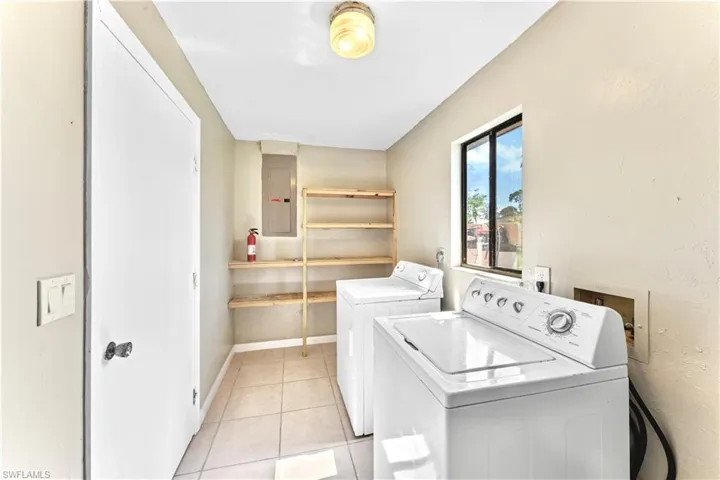 Clothes washing area featuring washer and dryer, electric panel, and light tile patterned floors