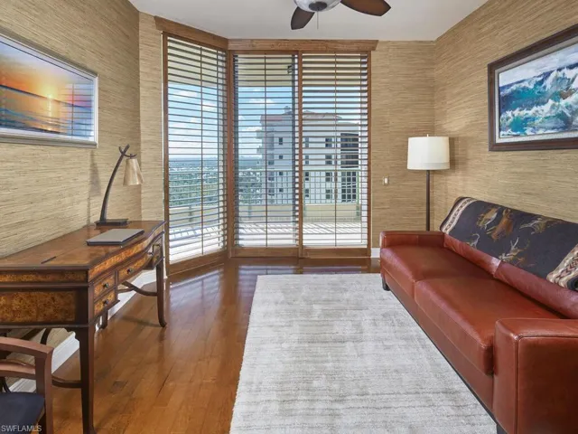Sitting room with wallpapered walls, ceiling fan, dark wood-type flooring, and an office area