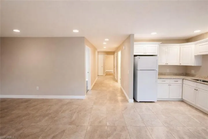 Kitchen featuring freestanding refrigerator, white cabinetry, light stone countertops, and recessed lighting