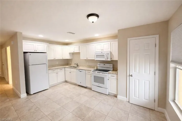 Kitchen with white appliances, white cabinets, recessed lighting, and light tile patterned flooring