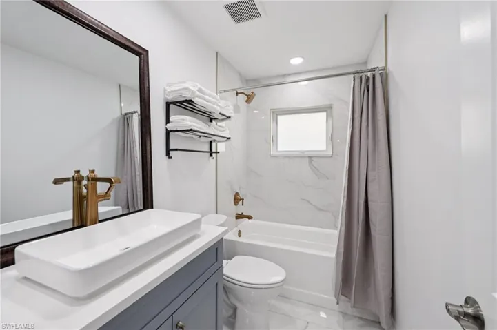 Bathroom with vanity, shower / bath combination with curtain, light marble finish floors, and recessed lighting