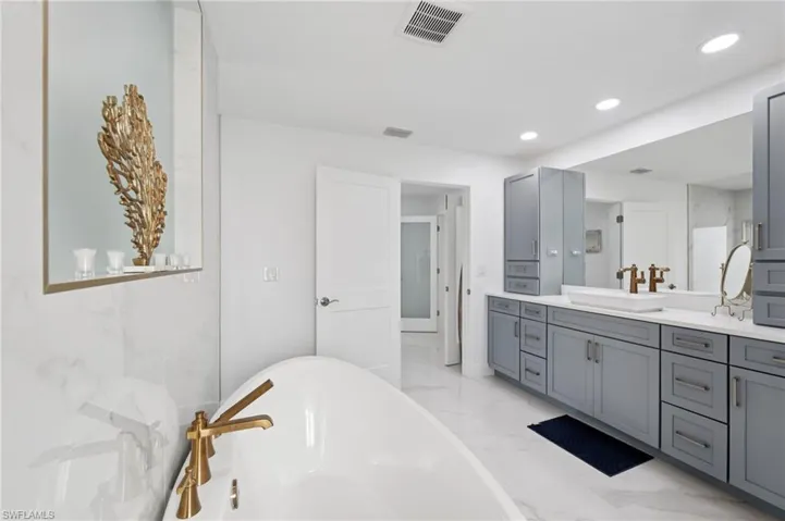 Bathroom featuring a freestanding tub, light marble finish floors, vanity, and recessed lighting