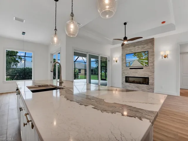 Kitchen featuring light stone counters, a raised ceiling, decorative light fixtures, and a fireplace