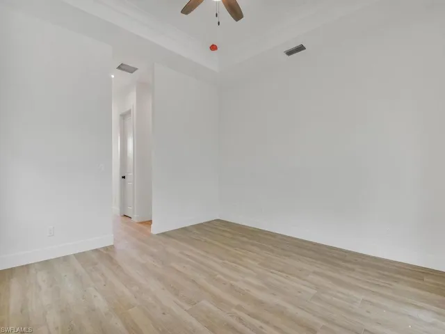 Spare room with light wood-style floors, crown molding, a raised ceiling, and ceiling fan