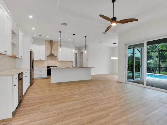 Kitchen featuring open shelves, white cabinets, decorative light fixtures, an island with sink, and ceiling fan