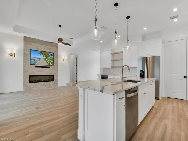 Kitchen featuring open floor plan, light stone countertops, white cabinets, a center island with sink, and open shelves