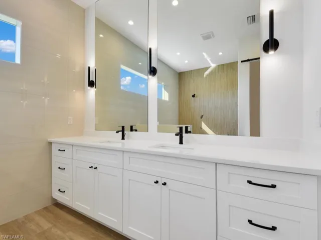 Bathroom featuring double vanity, a walk in shower, light wood-type flooring, and recessed lighting