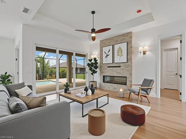 Living room featuring a raised ceiling, light wood-style flooring, a tile fireplace, and a ceiling fan