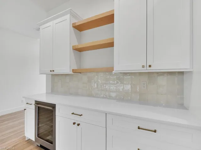 Bar area with tasteful backsplash, white cabinets, open shelves, and beverage cooler