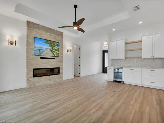 Unfurnished living room featuring a raised ceiling, light wood-style flooring, recessed lighting, beverage cooler, and ceiling fan