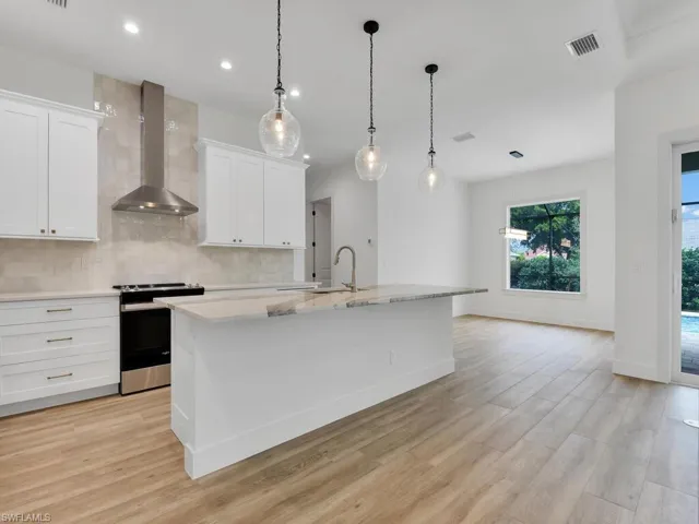 Kitchen featuring tasteful backsplash, stainless steel electric range oven, wall chimney range hood, light wood-style flooring, and white cabinets