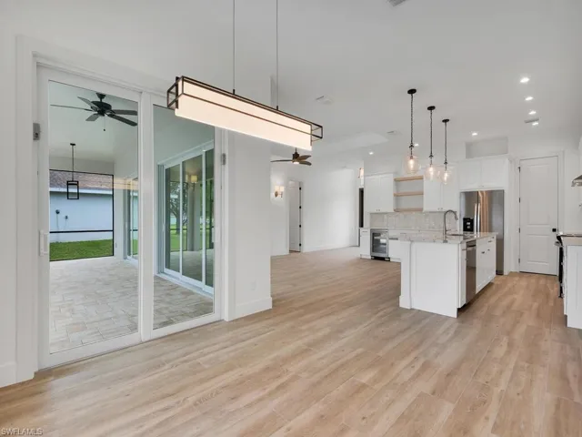 Kitchen featuring a ceiling fan, open floor plan, backsplash, decorative light fixtures, and light wood-style flooring
