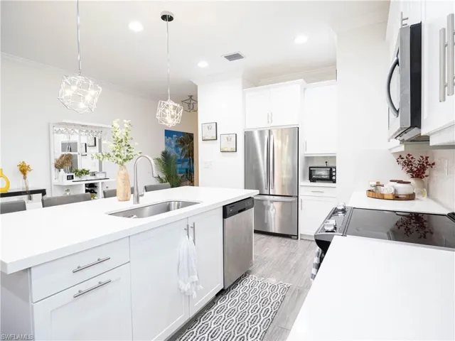 Kitchen with pendant lighting, sink, white cabinetry, stainless steel appliances, and ornamental molding