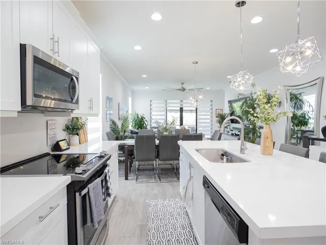 Kitchen with a center island with sink, appliances with stainless steel finishes, hanging light fixtures, and white cabinetry