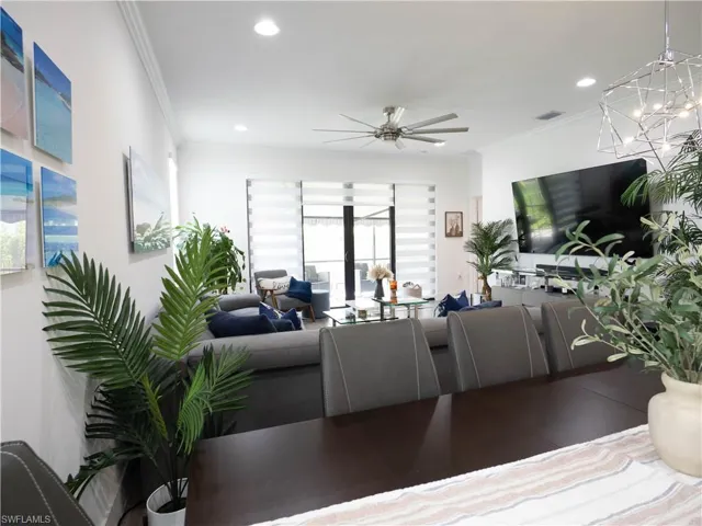 Living room featuring ceiling fan with notable chandelier and ornamental molding