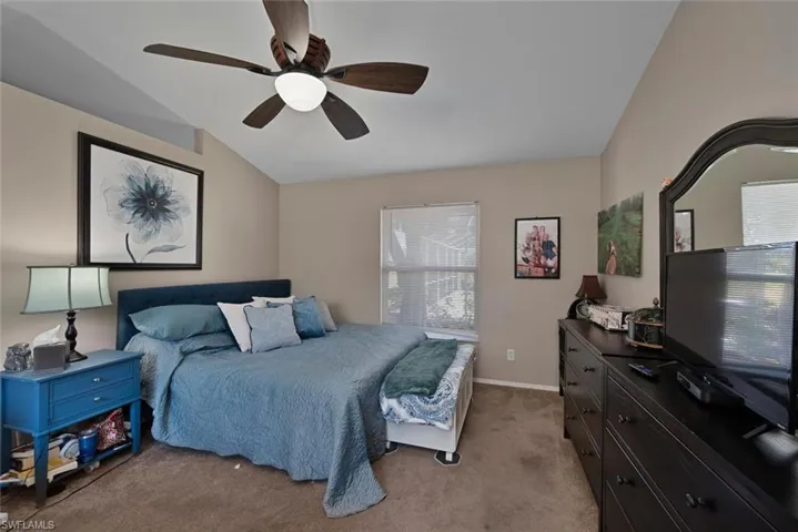 Carpeted bedroom with lofted ceiling, multiple windows, baseboards, and ceiling fan