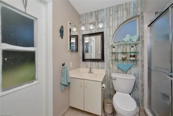 Full bathroom with toilet, a stall shower, wallpapered walls, and vanity