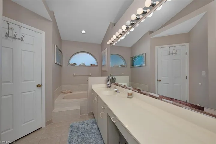 Full bath featuring tile patterned flooring, vanity, a garden tub, and vaulted ceiling