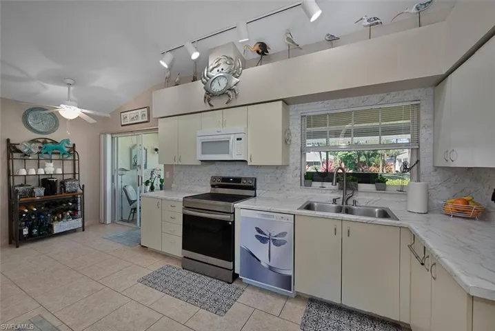 Kitchen featuring dishwashing machine, white microwave, stainless steel electric stove, a sink, and decorative backsplash