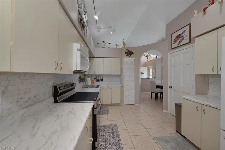 Kitchen with white microwave, backsplash, electric stove, and a sink
